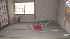 左角の畳の上には段ボール、部屋中央あたりの畳の上には赤い掃除機が置かれている2階和室の内観写真
