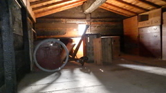 木の三角屋根のある小屋で右側にはタンスが置いてあり、奥には四角や丸い道具が収納されている土蔵の中の写真