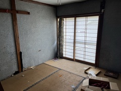 左側はコンクリートの壁、右奥には障子窓があり、畳の上に開けられている段ボールが置かれている和室の内観写真
