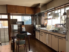 窓際に設置された白色の台所と端に置かれた木製の机と椅子の写真