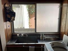 長方形の窓際に設置されたステンレス製の洗面所と脇に置かれた洗濯機の写真