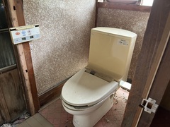 木枠が付いているコンクリートの壁とピンク色の床に洋式トイレが設置されているトイレの写真