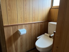 木の板の壁に囲まれた中に右側に洋式トイレ、左側にトイレットペーパーホルダーが設置されているトイレの中の写真