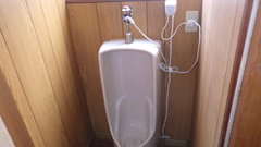 木の壁に囲まれた部屋に男性用の白い小便器があるトイレの中の写真