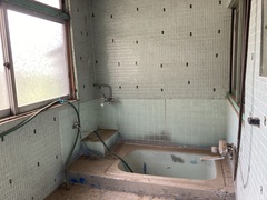 グレーと水色のタイルの壁に囲まれた浴室で左側には大きな窓があり、右奥にバスタブが設置されている浴室の写真