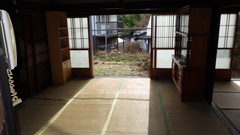 左側には木の扉、その前には棚が置いてあり、奥にある障子から光が差しこんでいる2間続きになっている和室の内観写真