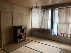 左側に小さな棚が置かれており、奥には大きな窓があり白とピンクのカーテンが設置されている2階和室の内観写真