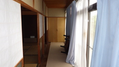 左に和室と境目に上部が障子したガラスの仕切りがあり、右側に大きな窓と水色のカーテンが設置されている1階廊下の写真