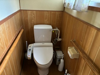 右側にトイレットペーパーホルダー、左右に手摺り、中央に洋式水洗便器があるトイレの写真