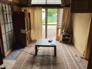 正面真中にテーブル、正面奥左側に食器棚、左側にガラス引き戸、正面奥にカーテンが左右に開き、障子戸、サッシ戸がある和室内観写真