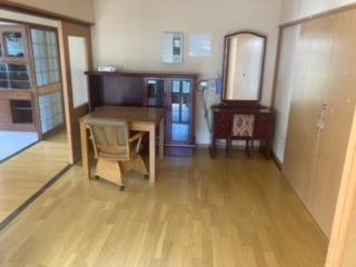 右側奥に鏡台、中央奥に茶ダンス、その手前に机、椅子、左側に廊下がある洋室内観写真