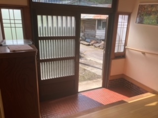 左側に下駄箱、中央に玄関引き戸、右側に手すりがある玄関の写真
