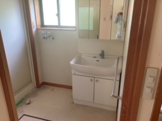 左側に浴室引き戸、中央奥上部にサッシ、右側に収納、鏡つき洗面台がある洗面所の写真