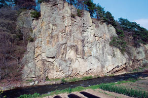 青い空のもと駒形岩が聳え立ち、その下には伊田川が流れている様子の写真